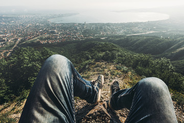 Man traveler sits on top and enjoys view of the picturesque landscape and the city. Point of view...