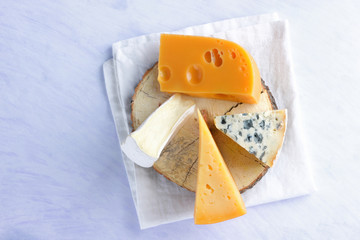 Camembert, hard yellow cheese and blue cheese on wooden board. Pieces of various cheeses on white napkin. Dorblu and soft cheese in style of minimalism. Dairy products