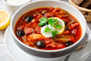 Traditional Russian meat soup Solyanka in bowl on rustic wooden table. Selective focus.