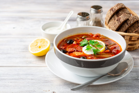 Traditional Russian meat soup Solyanka in bowl on rustic wooden table. Selective focus.