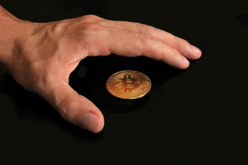 Fototapeta premium Hand of a young man with a gold bitcoin on a black background. Businessman defend bitcoin. Bitcoin concept.