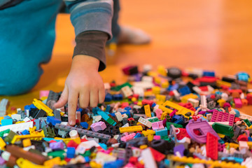 Close up of colorful plastic bricks on the floor. Early learning. Children's plastic constructor on the floor. Children's hands play a little constructor. vertical photo.