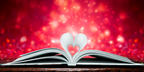 Book With Pages Curved Into Heart Shape On Wooden Table With Dazzling Red Background 