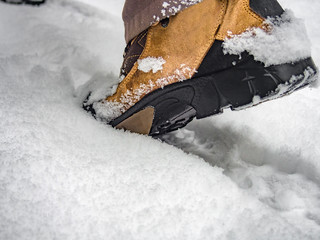 Winter hiking boots on the mountain trail. Closeup. Male walking in forest, focus on feet. Rear view.