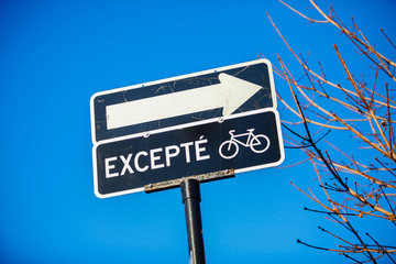One way road sign except for bikes. Closeup shot on the black sign with blue sky in the background. Shot in Montreal, Quebec, Canada