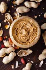 Homemade peanut butter in a glass jar on a wooden background with shells and nuts. Food stylish horizontal shot