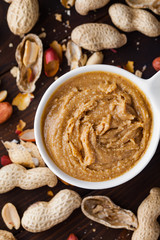 Homemade peanut butter in a white plate jar on a wooden background with shells and nuts. Food stylish horizontal shot