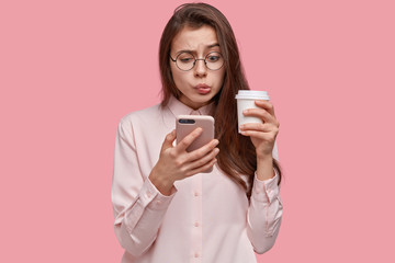 Studio shot of anxious puzzled cute lady reads message from ex boyfriend, reads weird information,...
