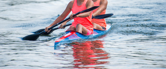 Two young woman athletes on rowing kayak on lake during competition
