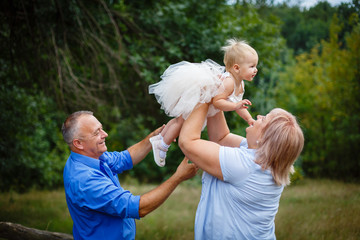 Portrait of adorable grandparents with her cute granddaughter walking in the park. Happy grand...