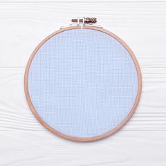 Fototapeta na wymiar Tools for cross stitch. A hoop for embroidery and canvas on white wooden background. Mockup about hobby