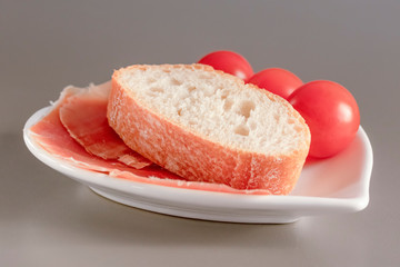 Dry Spanish ham, jamon, Italian ham, chopped layers with bread and cherry tomatoes on a white heart-shaped plate