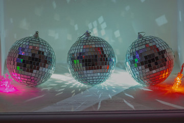 Three christmas tree toys shiny disco balls on a white background with reflections illuminated with a garland in the form of snowflakes