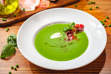 Green pea cream soup with bacon in white plate. Close up