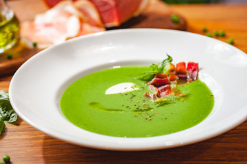 Green pea cream soup with bacon in white plate. Close up