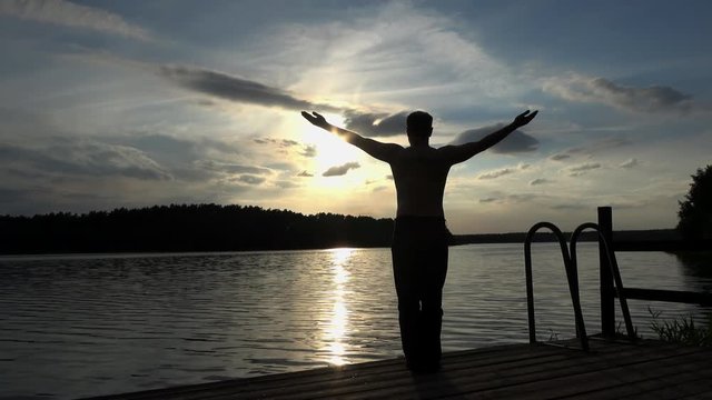 ein Mann steht bei Sonnenuntergang am See und macht Sport