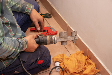 Plumber holds in his hand an apparatus for welding plastic pipes. On the floor lies a pipe cutter for polypropylene pipes.