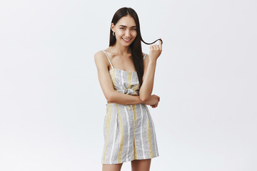 Yeah I am flirting with you. Good-looking fashionable and feminine woman in summer outfit playing with hair strand, rolling it on finger and smiling sensually at camera, seducing over grey wall