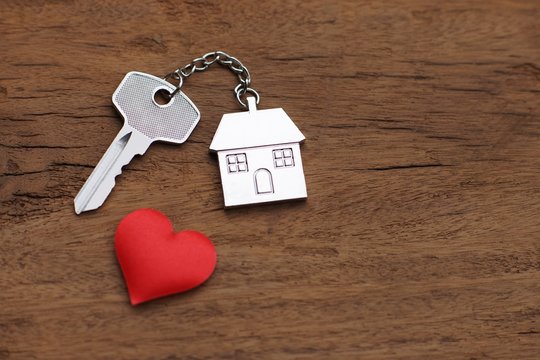 Home key with love house keyring decorate with mini heart on wood background, sweet home concept