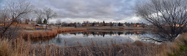 Fototapeta premium Views of Josh’s Pond walking path, Reflecting Sunset in Broomfield Colorado surrounded by Cattails, plains and Rocky mountain landscape during sunset. United States.