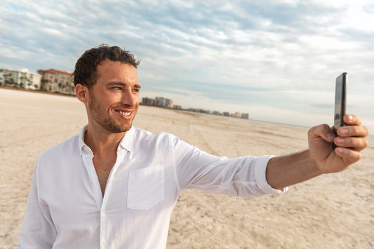 Selfie vacation beach man in white linen shirt taking photo with mobile phone on honeymoon travel vacation. Happy young using smartphone on holdiay.