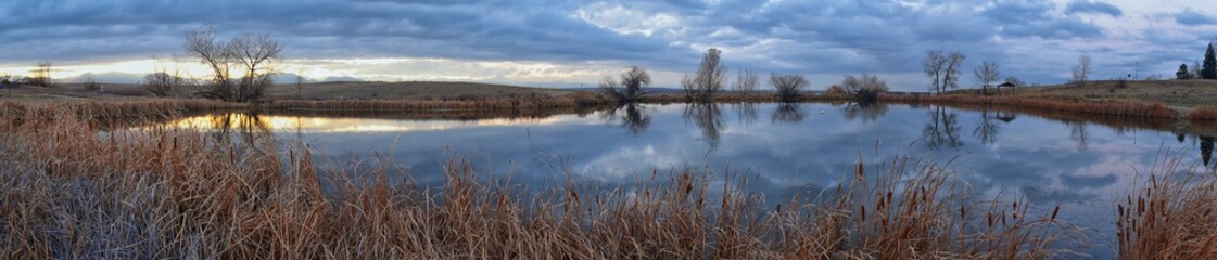 Views of Josh’s Pond walking path, Reflecting Sunset in Broomfield Colorado surrounded by Cattails, plains and Rocky mountain landscape during sunset. United States.