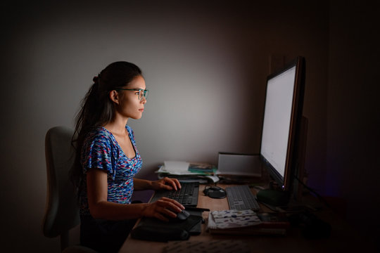 Working late at night on computer. Asian woman at office desk staring at desktop screen wearing blue light eyewear glasses to protect from eye strain for long hours of work.