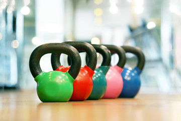 Naklejka na ściany i meble Colorful kettlebells in a row on the wooden floor in a gym. Rows of kettlebells in the gym.