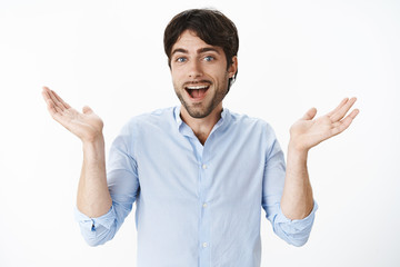 I do not give care. Portrait of unbothered and careless chill and happy young good-looking joyful man with blue eyes and beard shrugging with hands raised and spread sideways smiling pleased