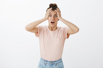 Studio shot of panicking woman realising forgot to send important email standing concerned with hands on head and opened mouth freaking out, overthinking looking intense and worried