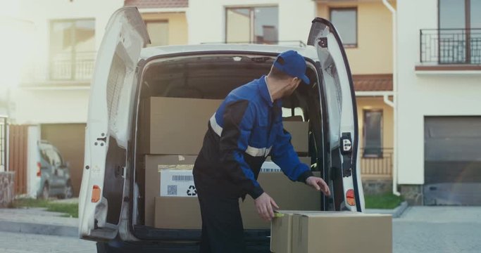 Handsome Caucasian male worker of the shipping company taking out carton parcels from the van.Outside.self isolation, shipping, transportation, quarantine,online, pandemic, food, package 
