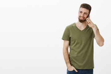 Studio shot of stylish and confident good-looking bearded male entrepreneur talking on smartphone smiling and laughing enjoying conversation looking at upper left corner over white background