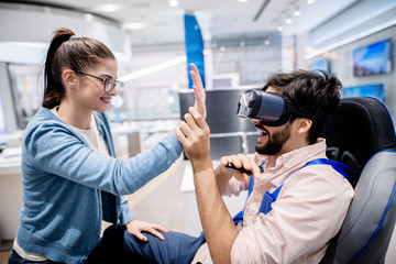 Amazed man using VR glasses holding woman`s hand. Woman crouching in front of him.