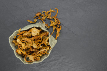 Top view composition of dry chanterelles mushrooms placed in canvas bag on black stone background...
