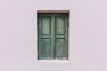 Old fashioned worn window with green wooden shutters, closed, on painted wall background.