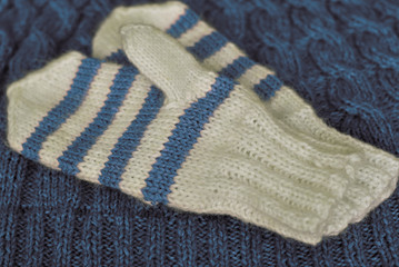 Fototapeta na wymiar Knit. Homemade knitted striped mittens on knitted pattern background. Blue colour.