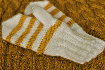 Knit. Homemade knitted striped mittens on knitted pattern background. Yellow.