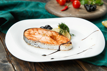 One piece of baked salmon grilled pepper lemon and salt on a brown plate with lettuce leaves. wood background