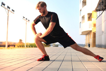 Handsome young man doing stretching exercises before running while standing outdoors.