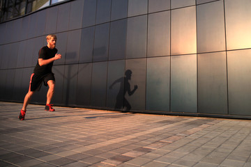Obraz na płótnie Canvas Sporty young man running outdoors to stay healthy, at sunset or sunrise. Runner.