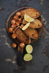 Fried fish cutlets with cherry tomatoes, lemon and lime, vertical shot on a brown stone background, above view