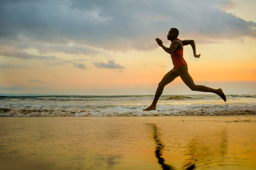 Fototapeta na wymiar silhouette of young attractive fit athletic and strong black African American man running at sunset beach training hard and sprinting on sea water in runner workout