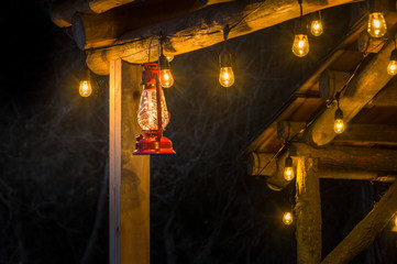 Red metal storm lantern hung outside rustic log cabin.
