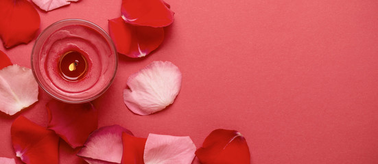 Candle and rose petals on red background. Banner format