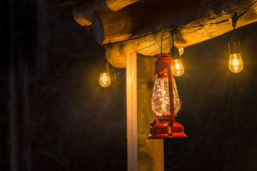 Red metal storm lantern hung outside rustic log cabin.