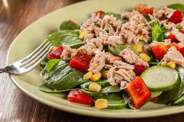 Fresh spinach salad with tuna, cucumber, corn, and red paprika on a plate