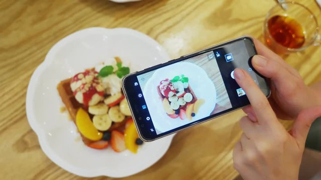 close-up. Female hands take a picture of a dessert of Viennese waffles, ice cream and fresh fruit on a smartphone in a restaurant.