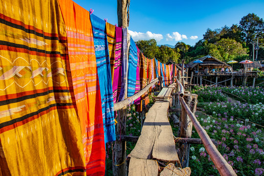 Thai Cultural Cotton Fabric Hanging Along Wooden Bridge Crossing Flower Field.