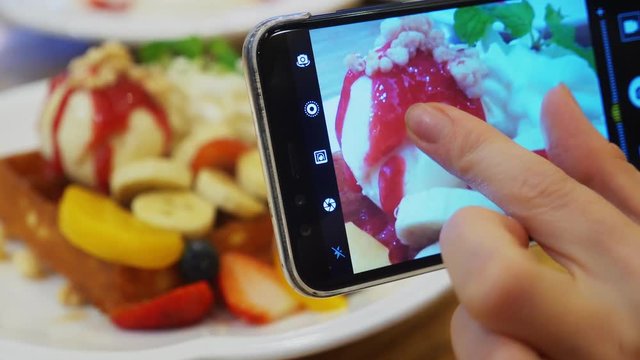 close-up. Female hands take a picture of a dessert of Viennese waffles, ice cream and fresh fruit on a smartphone in a restaurant.
