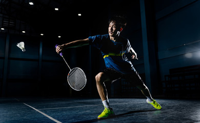 Asian badminton player is hitting in court - obrazy, fototapety, plakaty